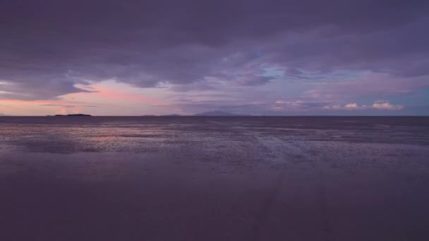 夕日にはウユニ塩フラッツ 空中展望 ボリビアのアルティプラノ 梅雨の季節 ツンパ火山 湖表面の水に雲の反射 ドローンは低レベルで後方に飛ぶ — ストック動画