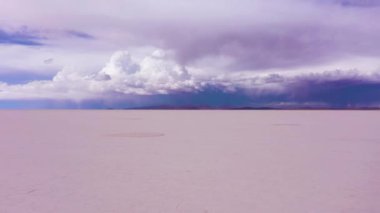 Güneşli bir günde Uyuni Tuz Düzlüklerine Bakan Yalnız Adam. Hava görüntüsü. Altiplano, Bolivya. Kurak Mevsim. Tuz oluşumları. Drone geriye doğru uçuyor. Geniş açı. Dramatik ve Fırtınalı Gökyüzü. Solo Seyahat Konsepti