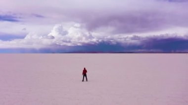 Gezgin adam güneşli bir günde Uyuni Tuz Düzlüklerine bakıyor. Hava görüntüsü. Altiplano, Bolivya. Kurak Mevsim. Tuz oluşumları. Drone İleri Uçuyor. Geniş açı. Dramatik ve Fırtınalı Gökyüzü. Solo Seyahat Konsepti