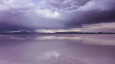 Adam ayakta duruyor ve Uyuni Tuz Düzlükleri 'ne bakıyor. Hava görüntüsü. Altiplano, Bolivya. Yağmur mevsimi. Suyun yansıması. Drone geriye doğru uçuyor. Geniş açı. Dramatik ve Fırtına Bulutları. Solo Seyahat Konsepti