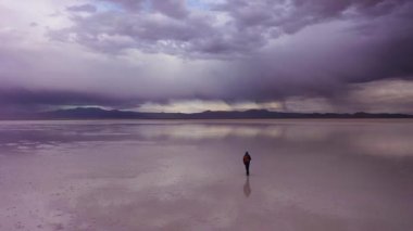 Turist Yürüyüşü. Uyuni Tuz Düzlükleri. Hava görüntüsü. Altiplano, Bolivya. Yağmur mevsimi. Suyun yansıması. Drone adamı takip ediyor. Aktif Atış. Dramatik ve Fırtına Bulutları. Solo Seyahat Konsepti