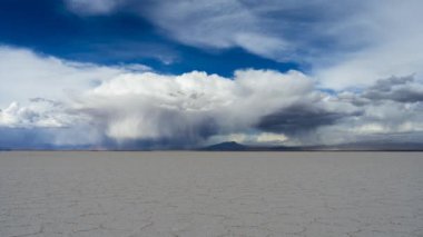 Güneşli bir günde Uyuni Tuz Düzlükleri. Salar De Uyuni. Altiplano, Bolivya. Kurak Mevsim. Dramatik Fırtına Bulutları geliyor. Altıgen Tuz oluşumları ve Çatlak desenleri. Geniş açı. Zaman Süreleri