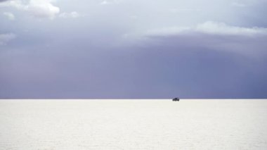 Bulutlu bir günde Uyuni Tuz Düzlükleri ve Yoldan geçen Araba. Bolivya