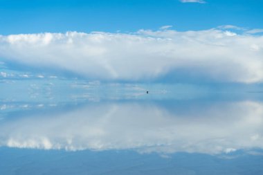 Uyuni Salt Flats 'da bir araba. Altiplano, Bolivya. Yağmur mevsimi. Tunupa Volkanı. Göl yüzeyinde Bulutların Yansıması