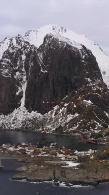 Kışın Hamnoy Balıkçılık Köyü ve Festhelltinden Dağı. Lofoten Adaları, Norveç manzarası. Hava görüntüsü. Drone yörüngede. Dikey Video