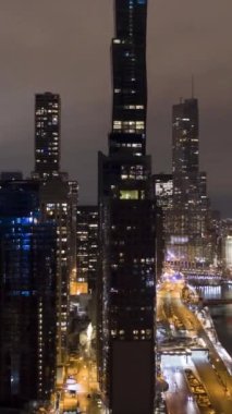 Şikago Şehri ve Chicago Nehri 'nin Kış Gecesi Şehir manzarası. New East Side ve Streeterville. Hava Hızı Hızı, Zaman Hızı. Amerika Birleşik Devletleri. İnsansız hava aracı yandan uçuyor. Dikey Video