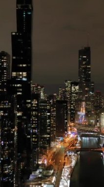 Chicago City 'nin Urban Skyline' ı ve kışın Gece Şikago Nehri. New East Side ve Streeterville. Hava görüntüsü. Amerika Birleşik Devletleri. Drone yörüngede. Dikey Video