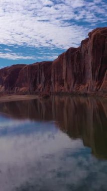 Güneşli bir günde Colorado Nehri ve Red Sandstone Kayalıkları. Wall Street Kaya Tırmanma Alanı. Sudaki Bulutlar Yansıması. Grand County, Utah, ABD. Hava görüntüsü. Drone geriye doğru uçuyor. Dikey Video