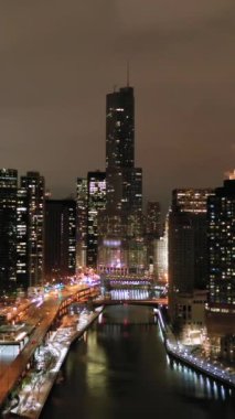 Urban Chicago City ve Chicago River, kışın Gece 'de. New East Side ve Streeterville. Hava görüntüsü. Amerika Birleşik Devletleri. Drone yukarı ve ileri uçuyor. Dikey Video