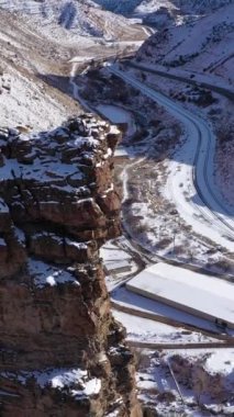 Güneşli kış gününde Kale Kapısı Kulesi. Karlı Dağlar ve Yol. Utah, ABD. Hava görüntüsü. İHA ileri uçar, aşağı eğilir. Dikey Video