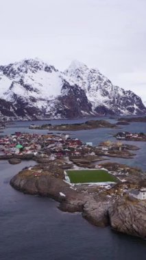 Kışın Henningsvaer Balıkçı Köyü ve Festvagtind Dağı. Norveç Denizi. Lofoten Adaları, Norveç manzarası. Hava görüntüsü. Drone yörüngede. Dikey Video