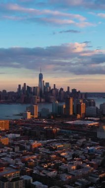 Aşağı Manhattan 'dan Urban Skyline, Jersey City ve Hudson River. New York, Sunset 'te. Binalarda güneş ışığı. Hava görüntüsü. Amerika Birleşik Devletleri. İnsansız hava aracı yandan uçuyor. Dikey Video
