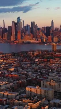 Manhattan şehir merkezinden Urban Skyline, Sunset 'ten Hoboken ve Hudson River. Binalarda güneş ışığı. New York City, ABD. Hava görüntüsü. İnsansız Hava Aracı Yana Uçuyor, Eğil. Dikey Video