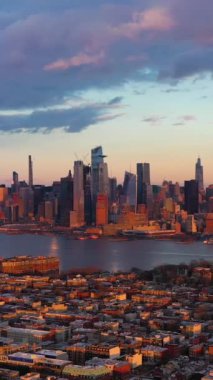 Manhattan şehir merkezinden Urban Skyline, Sunset 'ten Hoboken ve Hudson River. Binalarda güneş ışığı. New York City, ABD. Hava görüntüsü. İnsansız hava aracı yandan uçuyor. Dikey Video
