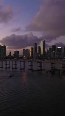 Miami, Akşam Alacakaranlığı 'nda. Şehir merkezi ve Rickenbacker Geçidi. Mavi Saat. Kentsel Şehir Manzarası. Hava görüntüsü. Florida, ABD. Drone ileri ve yukarı doğru uçuyor. Dikey Video