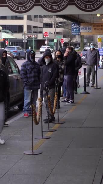 米国シアトル February 2021年 マスクを着用している人々はサイドウォークに並び コロナウイルスパンデミック中にカフェに入るのを待っている社会的距離を実践しています パイク プレイス バーティカルビデオ — ストック動画