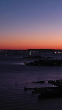 Akşam Alacakaranlığı 'nda Aydınlanmış Özgürlük Heykeli ve Verrazzano Köprüsü. Mavi Saat. Hava görüntüsü. New York City, ABD. Dikey Video