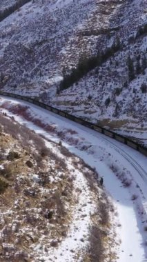 Güneşli kış gününde Yük Treni ve Karlı Dağlar. Kar yağıyor. Utah, ABD. Hava görüntüsü. Drone İleri Uçuyor. Dikey Video