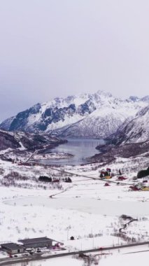 Kışın dağlar. Lofoten Adaları, Norveç manzarası. Hava görüntüsü. İnsansız hava aracı yukarı ve geri uçuyor. Dikey Video