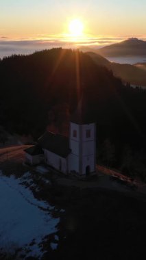 St. Primoz Kilisesi ve Felicijan Bulutların Üzerinde Gündoğumunda. Julian Alps. Jamnik, Slovenya, Avrupa. Hava görüntüsü. İnsansız hava aracı yukarı ve geri uçuyor. Dikey Video