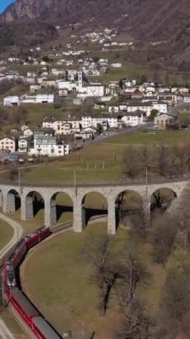 Güneşli bir günde İsviçre 'de Spiral Viaduct' ta tren. Bernina Demiryolu. İsviçre Alpleri. Hava görüntüsü. Drone İleri Uçuyor. Dikey Video