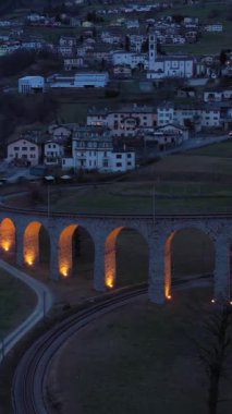 İsviçre 'deki Aydınlatılmış Spiral Viaduct Treni. Bernina Demiryolu. İsviçre Alpleri. Hava görüntüsü. Yörüngede. Dikey Video