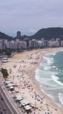 Güneşli bir günde Rio de Janeiro 'da. Copacabana Sahili ve Atlantik Okyanusu. Hava görüntüsü. Brezilya. İnsansız hava aracı Avenida Atlantica üzerinde ilerliyor. Dikey Video