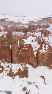 Kışın Kapadokya Peyzajı. Karlı Tepeler ve Sütunlar. Hindi. Hava görüntüsü. Drone Yörüngede, Eğil. Dikey Video