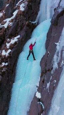 Donmuş Şelaleye Buz Tırmanışı. Dağcı Kadın, Buza öncülük ediyor. Havadan Yukarıdan Aşağı Görünümü. Barskoon Vadisi, Kırgızistan. İnsansız hava aracı aşağıya doğru uçuyor, yukarı doğru. Turna Vuruşu. Dikey Video