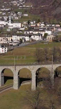 Güneşli bir günde İsviçre 'de Spiral Viaduct' ta tren. Bernina Demiryolu. İsviçre Alpleri. Hava görüntüsü. İnsansız hava aracı yukarı ve geri uçuyor. Dikey Video