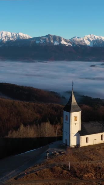在阴云之上的太阳日 圣普里莫兹教堂和Felicijan教堂 朱利安 阿尔卑斯山 Jamnik Slovenia Europe 空中景观 无人机向后和向上飞去 垂直录像 — 图库视频影像