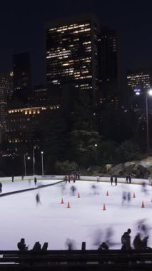 İnsanlar akşam saatlerinde Central Park 'ta buz pateni pistinde buz pateni yapıyorlar. Şehir merkezi şehir manzarası. - Manhattan. New York City, ABD. Zaman aşımı. Dikey Video