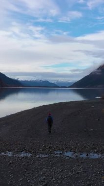 Portage Gölü kıyısında yürüyen adam. Güneşli bir günde karla kaplı dağlar. Alaska, ABD. Hava görüntüsü. Dikey Video
