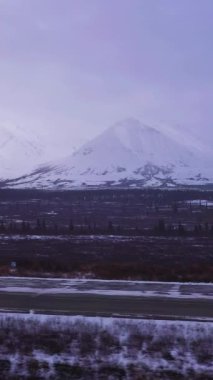 Kar yağışı sırasındaki Bulutlu Kış Günü 'nde Parklar Otobanı' nda ve Karlı Dağlar 'da araba. Alaska manzarası, ABD. Hava görüntüsü. İnsansız hava aracı yandan uçuyor. Dikey Video