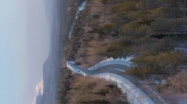 Kış gününde araba yolda. Karla kaplı dağlar. Hava görüntüsü. Murmansk Bölgesi, Kola Yarımadası, Rusya. Drone İleri Uçuyor. Dikey Video