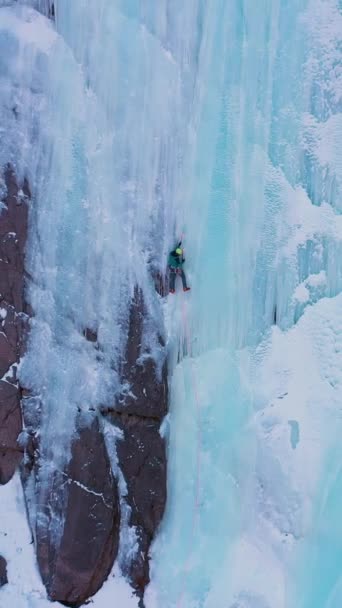 冰层爬上冰冷的瀑布 空中风景 登山者是领先的冰 吉尔吉斯斯坦的Barskoon Valley 无人机向后飞去 垂直录像 — 图库视频影像