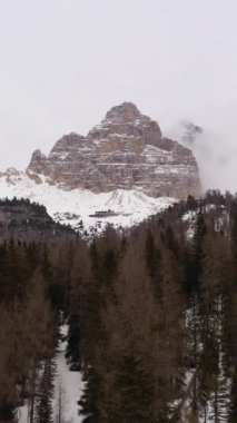 Tre Cime Di Lavaredo. Bulutlu Kış Günü ve Ormandaki Üç Tepe. Hava görüntüsü. Seksi Dolomitler, Güney Tyrol. İtalya. Drone ağaçların üzerinden uçuyor. Güney manzaralı. Dikey Video