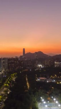 Sunset 'te parlayan Santiago City. Hava Hızı Hızı, Zaman Hızı. Akşam Alacakaranlığı. Mavi Saat. Las Condes Komünü. Şili. Drone Yana ve Yukarı Uçuyor. Dikey Video