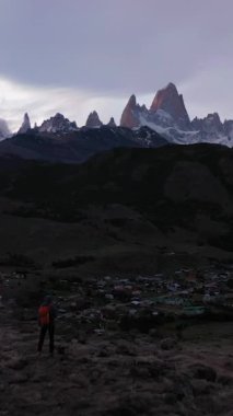 Turuncu Sırt çantalı Adam Fitz Roy Dağı ve Cerro Torre Dağı 'na bakıyor. El Chalten Town ve Las Vueltas Nehri. And Dağları, Patagonya, Arjantin. Hava görüntüsü. Dikey Video