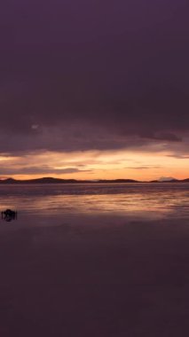 Sunset 'te Uyuni Salt Flats ve SUV Car. Hava görüntüsü. Altiplano, Bolivya. Yağmur mevsimi. Göl yüzeyindeki su yansıması. Drone İleri Uçuyor. Dikey Video