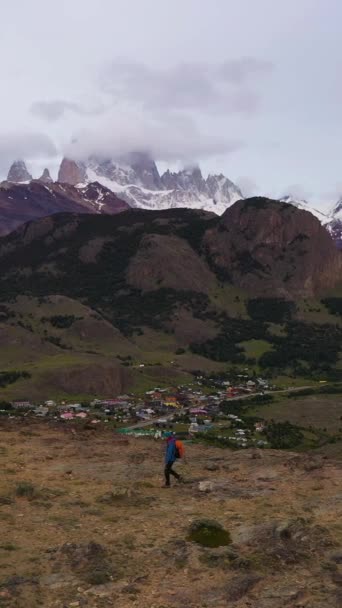 带着橙色背包的徒步旅行者走着 望着云雾中的菲茨罗伊山和圣杯镇 山与山 安第斯 巴塔哥尼亚 阿根廷 空中景观 博士飞的西道 垂直录像 — 图库视频影像