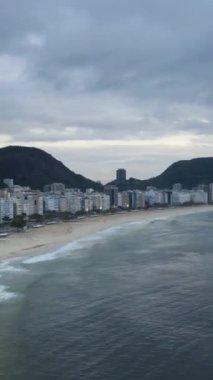 Rio de Janeiro City Skyline Bulutlu Sabah 'da. Copacabana Sahili ve Atlantik Okyanusu. Hava Hızı Hızı, Zaman Hızı. Brezilya. Drone ileri ve yukarı doğru uçuyor. Dikey Video