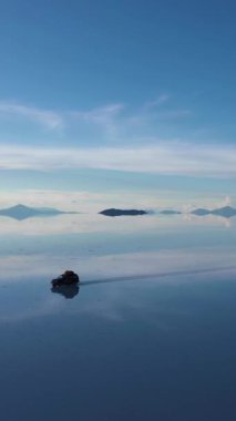 Güneşli bir günde Uyuni Tuz Düzlükleri. Salar De Uyuni. Hava görüntüsü. Altiplano, Bolivya. Islak Mevsim. SUV arabası. Göl yüzeyinde Bulutların Yansıması. Yörüngede. Dikey Video