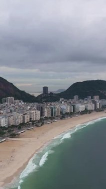 Rio de Janeiro City Skyline Bulutlu Sabah 'da. Copacabana Sahili ve Atlantik Okyanusu. Hava görüntüsü. Brezilya. İnsansız hava aracı yukarı ve geri uçuyor. Dikey Video