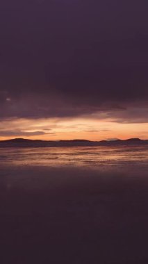 Sunset 'teki Uyuni Tuz Düzlükleri. Salar de Uyuni. Hava görüntüsü. Altiplano, Bolivya. Yağmur mevsimi. Göl yüzeyindeki su yansıması. İnsansız hava aracı alçaktan uçuyor. Dikey Video