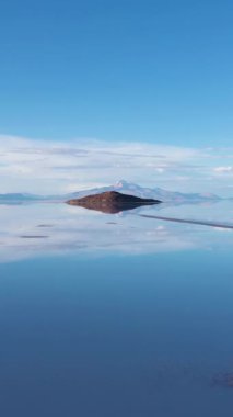 Uyuni Tuz Düzlükleri. Hava görüntüsü. Altiplano, Bolivya. Yağmur mevsimi. Tunupa Volkanı ve Incahuasi Adası. Göl yüzeyinde Bulutların Yansıması. Drone ileri ve yukarı doğru uçuyor. Dikey Video