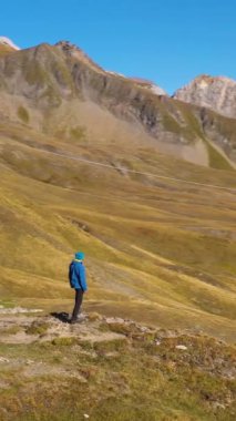 Mavi ceketli yürüyüşçü dağlara doğru bakıyor. Tepeler ve Dağlar. Albay Croix du Bonhomme. Fransız Alpleri, Fransa. Hava görüntüsü. Yörüngede. Orta boy shot. Dikey Video