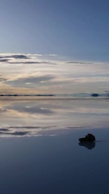 Uyuni Tuz Düzlükleri. Salar De Uyuni. Hava görüntüsü. Altiplano, Bolivya. Islak Mevsim. SUV arabası. Göl yüzeyinde Bulutların Yansıması. İnsansız hava aracı yandan uçuyor. Dikey Video