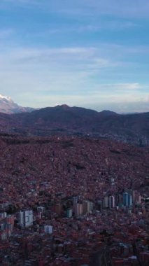 La Paz Cityscape ve Illimani Dağı. Hava görüntüsü. Bolivya 'da. Altın Saat. İnsansız hava aracı yandan uçuyor. Geniş açı. Dikey Video