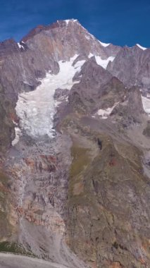Mavi ceketli yürüyüşçü güneşli bir günde Mont Black Mountain 'a bakıyor. İtalyan Alpleri, İtalya. Hava görüntüsü. Drone geriye doğru uçuyor. Dikey Video